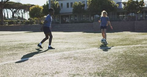 Sunlit youth soccer practice on school turf with two players dribbling
