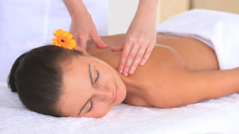 Relaxed Woman Enjoying Massage with Orange Flower in Spa