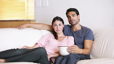 Cute Couple Relaxing on Couch Watching TV with Bowl in Hand