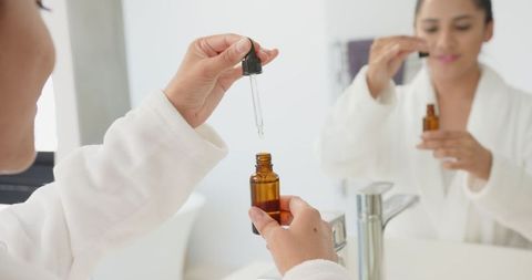 Woman applying serum dropper by bathroom mirror