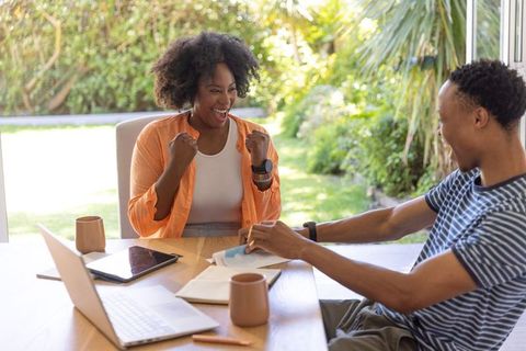 African american couple celebrating winning news at sunlit home table with laptop
