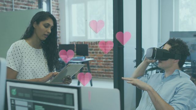 In an office setting, professionals are interacting with advanced technology. A woman holding a tablet collaborates with a man wearing a VR headset, suggesting a modern approach to teamwork. Pink heart icons add an element of creativity and visual emphasis, making it suitable for themes of innovation, modern workplace culture, and technology-driven interactions. Useful for content related to business transformation, tech startups, or promotional material for VR products.