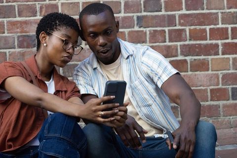 Young couple sharing phone moment while laughing and discovering content outdoors