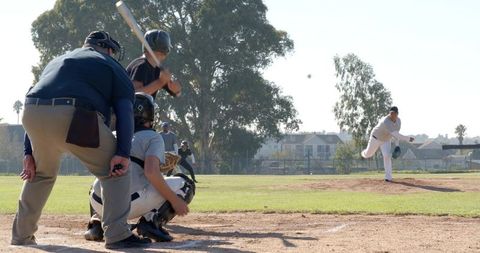 Pitcher pitching fastball as batter swings at home plate with catcher and umpire crouching