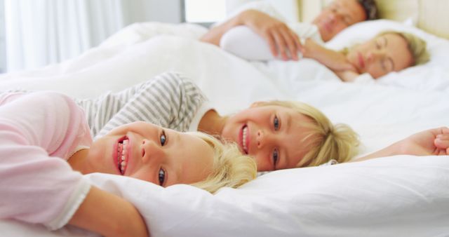 Happy Blonde Sisters Smiling in Bed with Parents Sleeping in Background - Download Free Stock Images Pikwizard.com