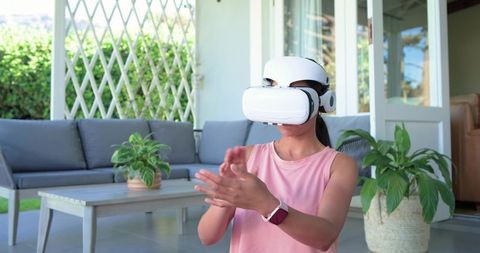 African American woman using VR headset and smartwatch on modern covered patio with plants