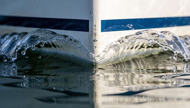 Boat bow slicing calm water creating mirrored ripples and glassy spray