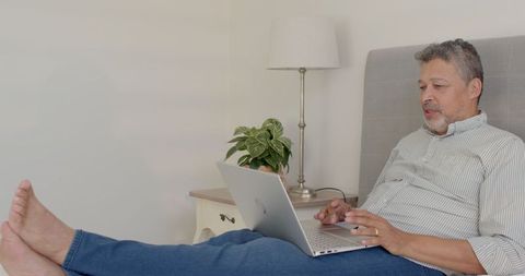 Senior Man Relaxing on Bed Using Laptop for Video Call at Home