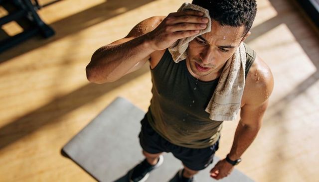 Sunlit gym athlete wiping sweat with towel after intense workout on gray mat