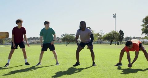 Multiracial men practicing drill on sunny field reacting to swinging tackle board