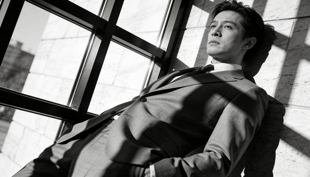 Contemplative Asian Executive Leaning and Gazing Through Metal Grid Window Shadows
