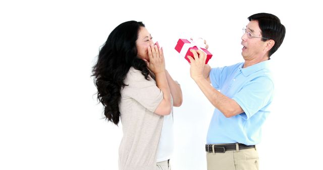 A middle-aged Asian man surprises a woman with a gift, both expressing joy and excitement, with copy space. Their delighted reactions suggest a special occasion or celebration.