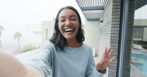Smiling Woman Enjoying Balcony View Overlooking Pool and Cityscape