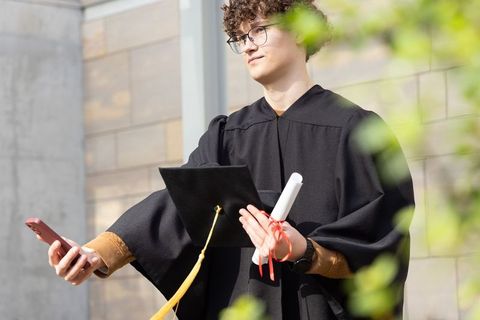 Young graduate taking selfie with cap and diploma outside modern university facade