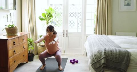 Pregnant Woman Exercising with Squats in Cozy Bedroom