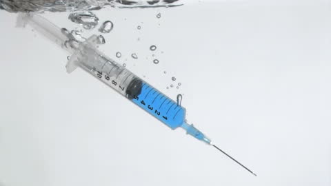 Syringe Making Splash in Water on White Background