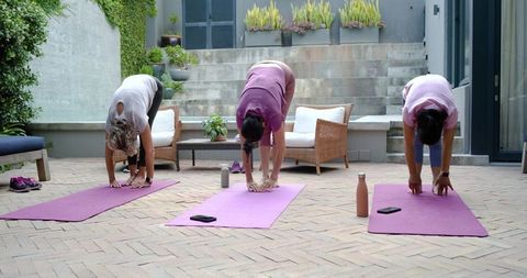 Diverse women practicing yoga and stretching on paved patio with purple mats