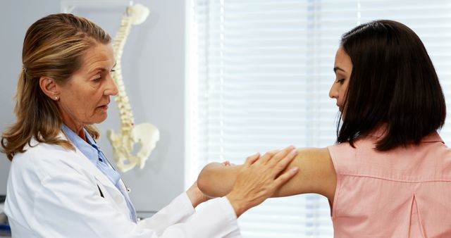 Female doctor examining patient's elbow in clinic. Useful for healthcare, medical practices, doctor-patient consultations, medical diagnostics, and health assessments.