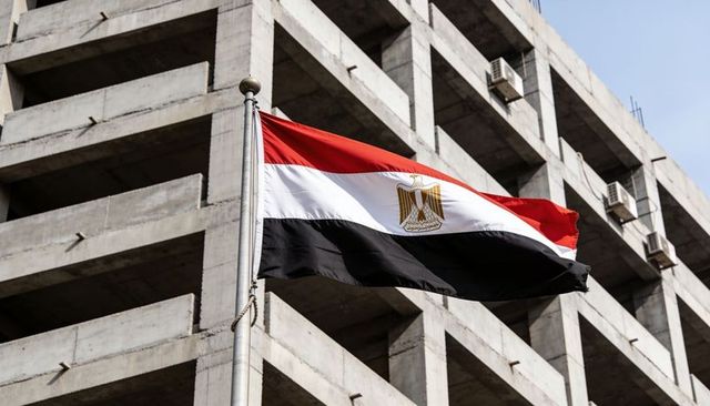Egyptian flag waving over concrete urban facade with golden eagle emblem and blue sky