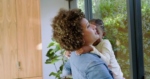 Mother Holding Child While Looking Out Glass Door in Modern Living Room