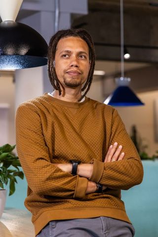 African american man leaning on counter in modern coworking lounge wearing rust sweatshirt