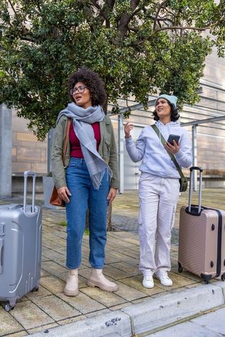 Two female travelers standing and chatting with luggage in urban plaza winter travel