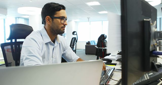 Man sitting at desk working on computer in bright modern office. Useful for projects related to business, technology, workplace efficiency, corporate lifestyle, and tech-savvy professionals.