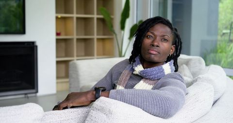 African american man relaxing on contemporary sofa wearing knitted scarf and smartwatch