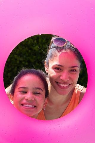 African american mother and daughter smiling through pink inflatable pool ring in backyard