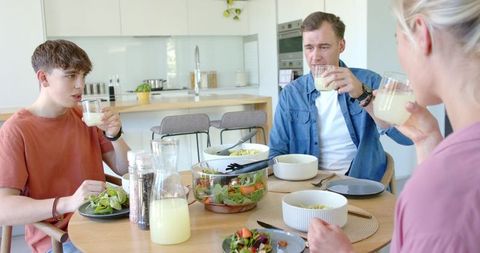 Family sharing healthy lunch around sunlit modern kitchen table, drinking lemonade