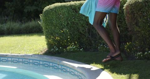 African american man stepping at pool edge with towel wearing pink and blue swim trunks