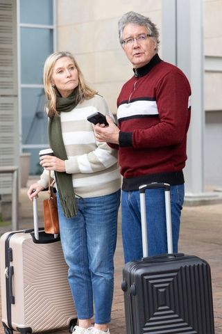 Senior couple waiting at station with luggage and smartphone, travel retirement lifestyle