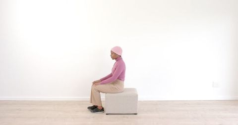 Woman Sitting in Minimalist Room Wearing Pink Sweater and Beanie