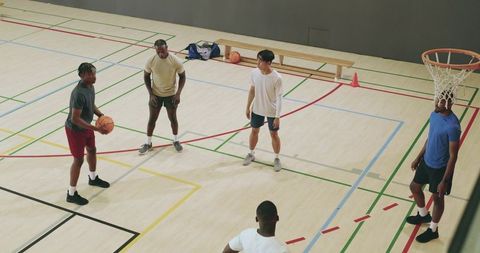 Diverse male friends playing pickup basketball passing and shooting on indoor gym court showing team