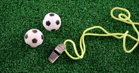 Miniature soccer balls and referee whistle on green field