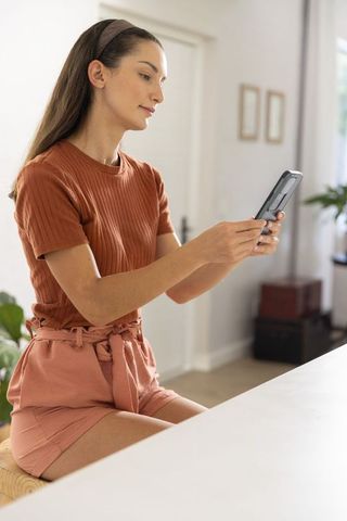 Young woman sitting at counter holding smartphone in bright minimalist home