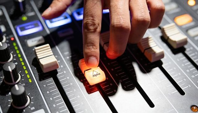 Pressing illuminated alpha fader on studio audio mixing console close-up with hand