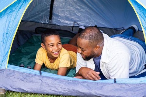African american father and son sharing laughter camping inside tent on grass