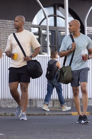 African american men walking with duffel bags and drinks on urban sidewalk