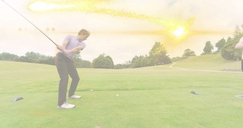 Male golfer swinging driver on sunlit tee with lens flare over fairway