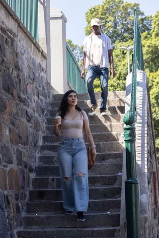 Urban couple walking down stone steps holding coffee cup and smartphone in warm sunlight