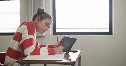 Focused student using tablet and notebook in classroom