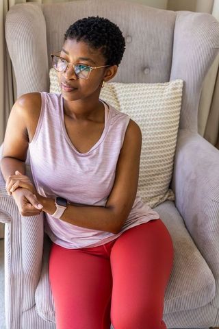 Woman sitting in wingback chair wearing pink top and red leggings touching smartwatch