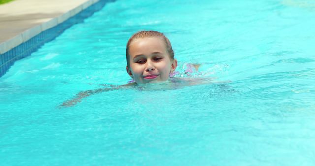 A young girl smiling while swimming in an outdoor pool during a sunny day. Ideal for use in content related to summer activities, children's sports, outdoor fun, vacation time, and family recreation. Can be featured in advertisements, blogs, travel agencies, and health or fitness campaigns.