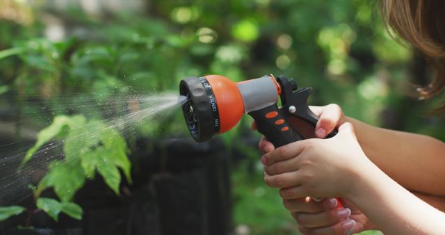Close up of hands of caucasian mother and daughter holding hose and watering plants in sunny garden. Family, nature, gardening and hobbies.