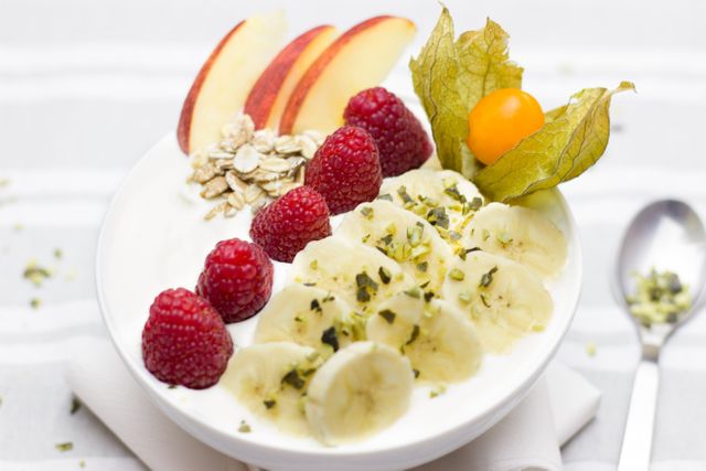 A nutritious yogurt bowl containing fresh bananas, raspberries, apples, and topped with a sprinkle of oats. Perfect for promoting a healthy lifestyle, diet, and nutritious eating habits. Ideal for websites and blogs focusing on healthy breakfasts, wholesome diets, and balanced nutrition.