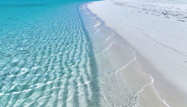 Sunlit turquoise shallows lapping pristine white sand beach with crystal clear ripples