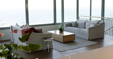 Coastal loft living room overlooking ocean, minimalist gray sofas with low wood coffee table