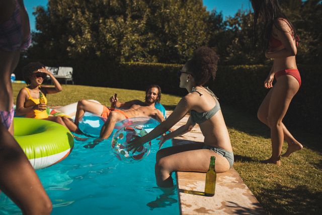Diverse group of friends sitting by the pool and in inflatable chairs sunbathing drinking beer. hanging out and relaxing outdoors in summer.