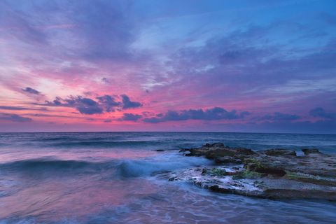 Lavender Sunrise Painting Sky Above Rocky Shore With Soft Waves And Coastal Calm